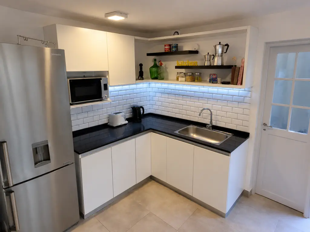 Cocina con muebles blancos, mesada oscura, revestimiento tipo subway e iluminación bajo alacena